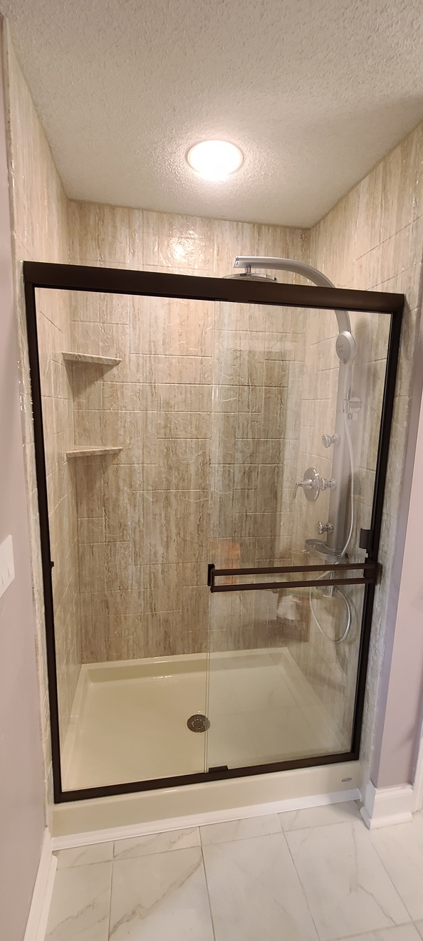 Walk-in shower with travertine-look tile walls and oil-rubbed bronze glass frame