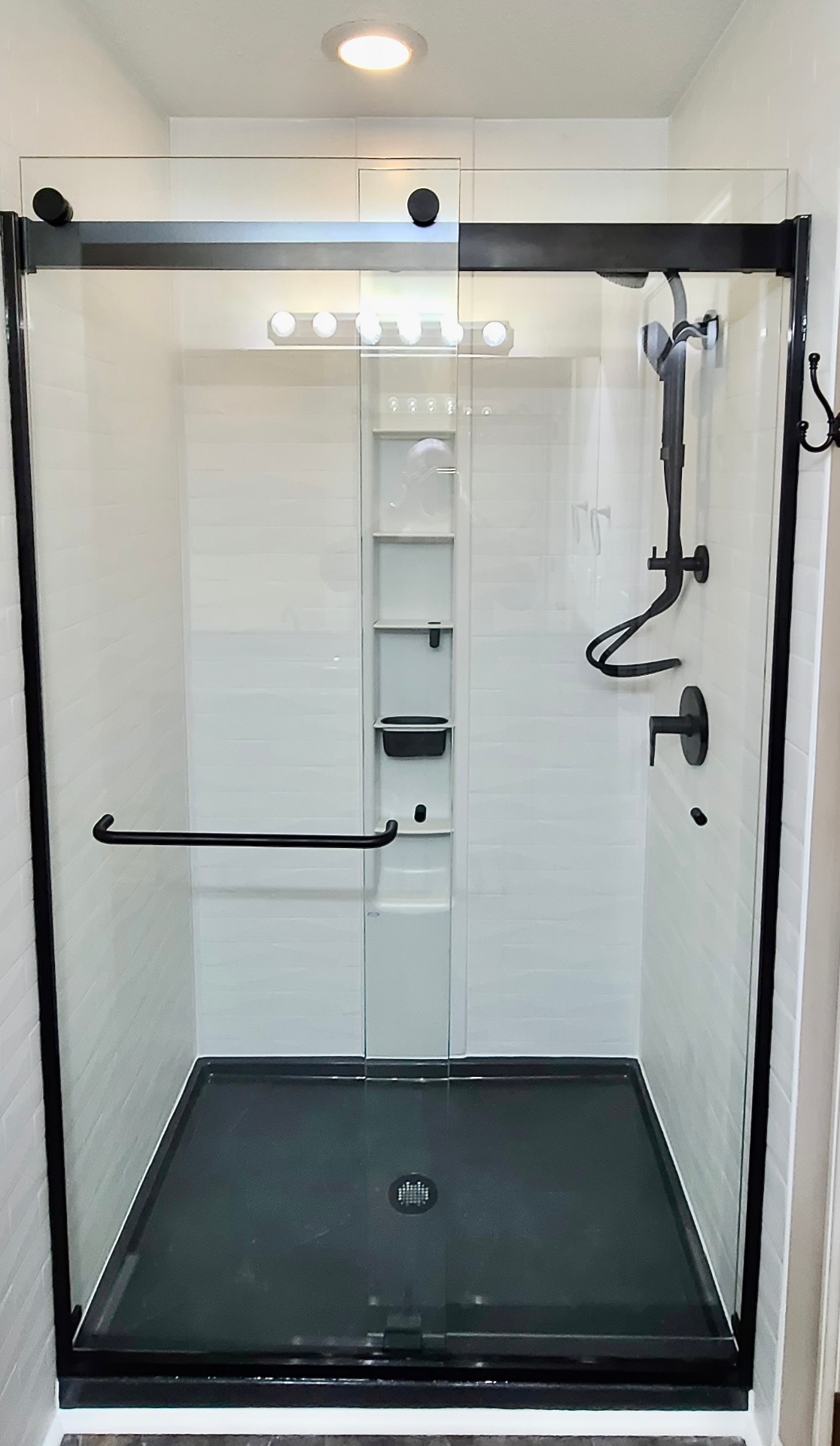 White subway-look shower with matte-black frameless sliding glass and black fixtures