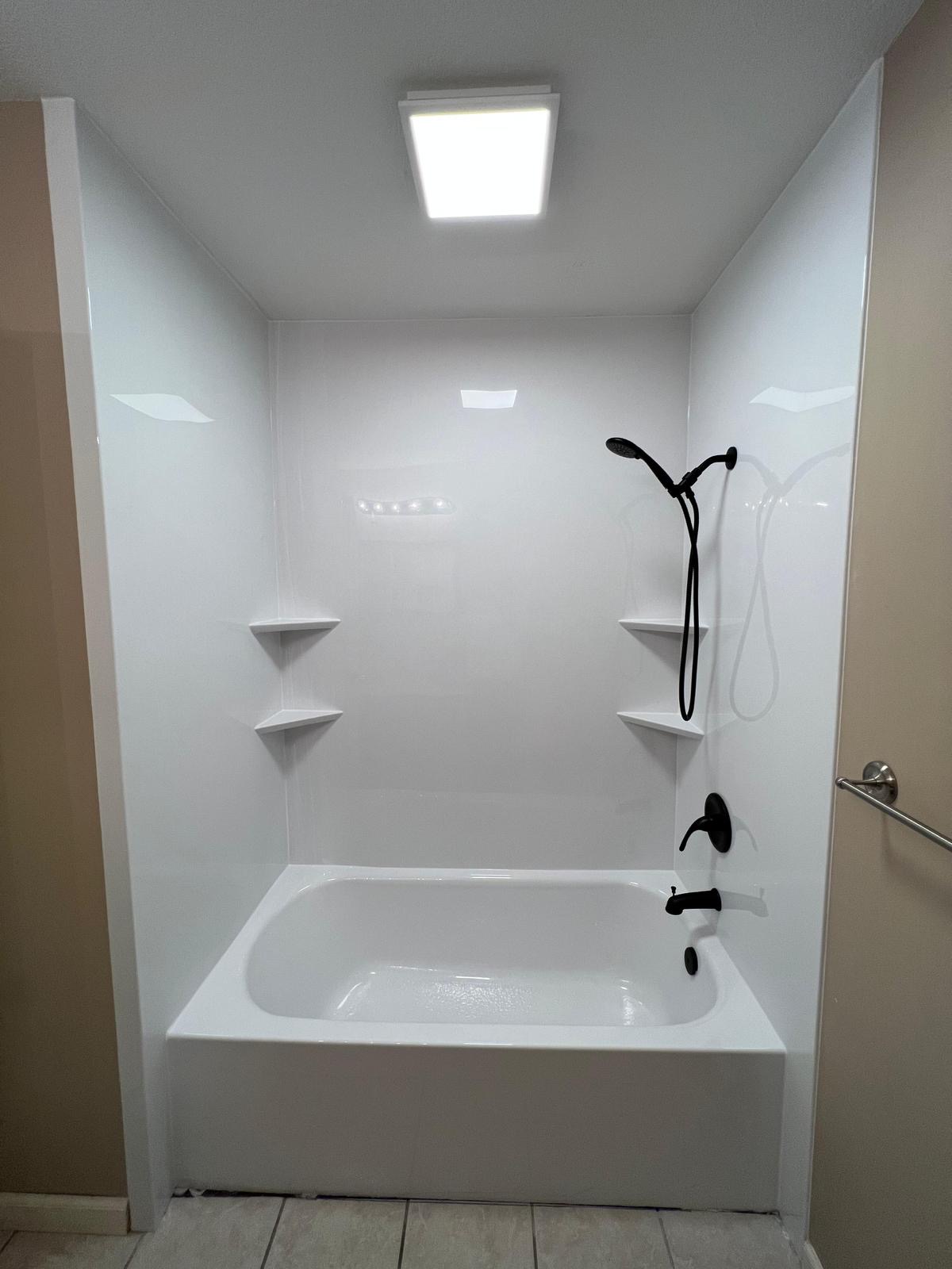 White acrylic tub-shower combo with matte black fixtures and corner shelves