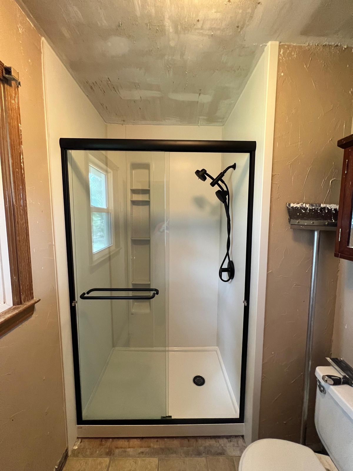 Walk-in shower with matte-black framed sliding glass door and grab bar