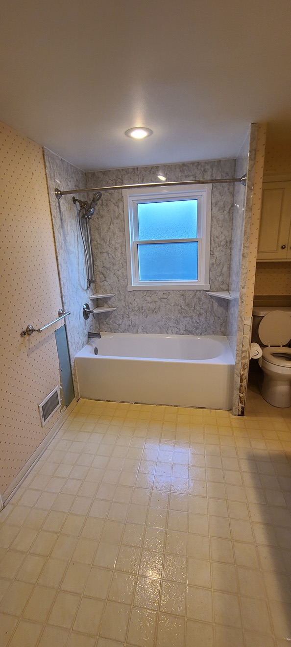 Original dated bathroom with old marble-look tub surround and wallpaper